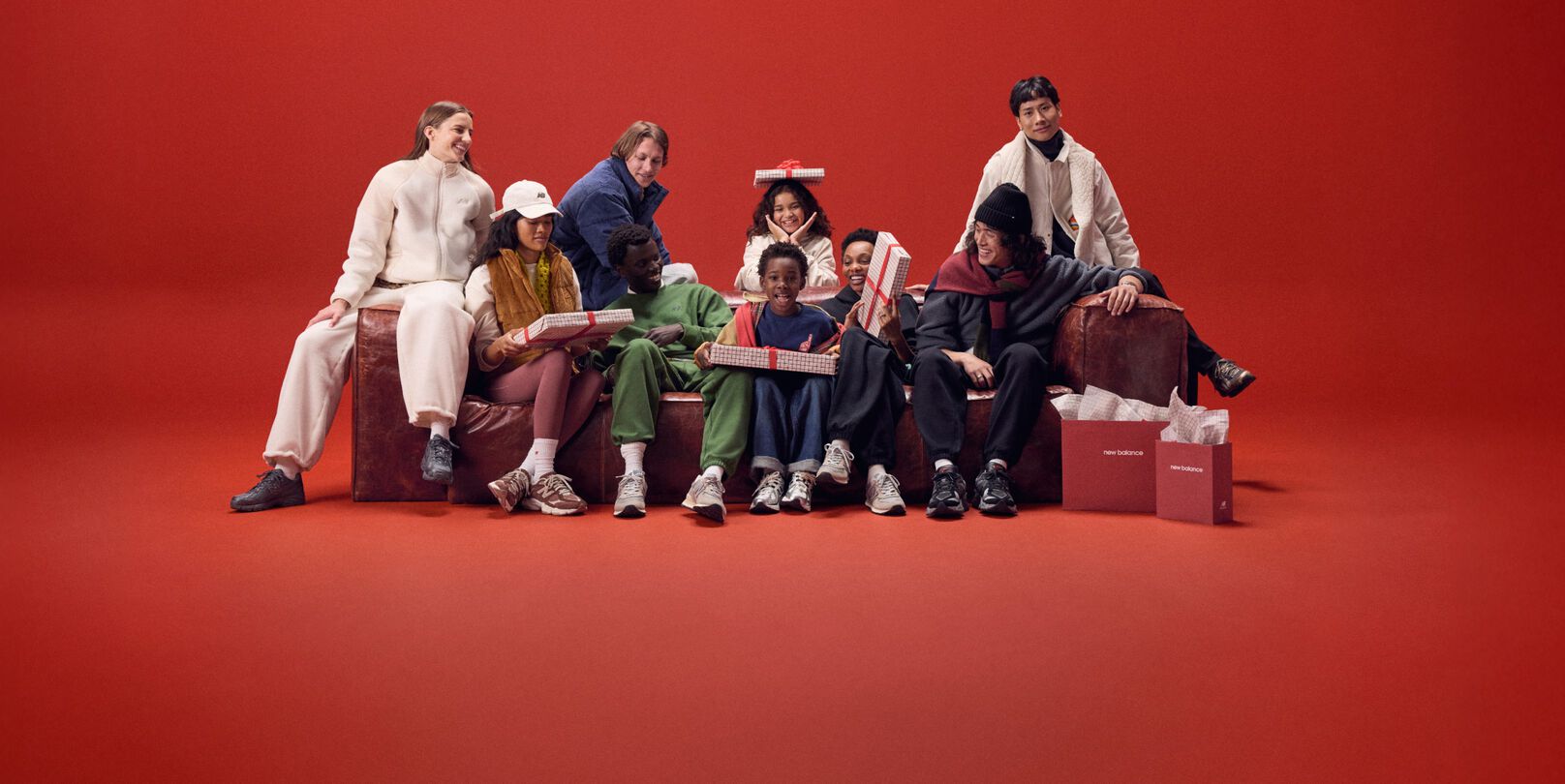 A group of people wearing New Balance sitting on a sofa with a red background.