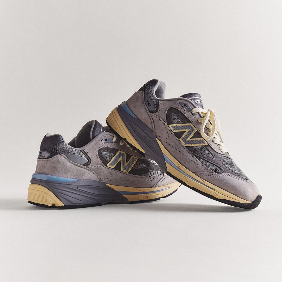 A pair of grey 990v7 sneakers sitting on a grey studio backdrop.