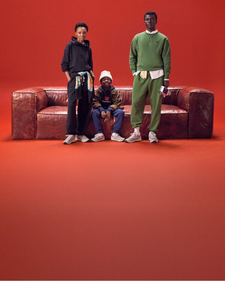 A group of people wearing New Balance standing next to a sofa with a red background.