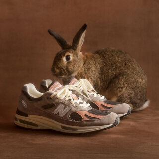 A pair of New Balance Made in UK sneakers in front of a rabbit in a brown textured studio environment. 