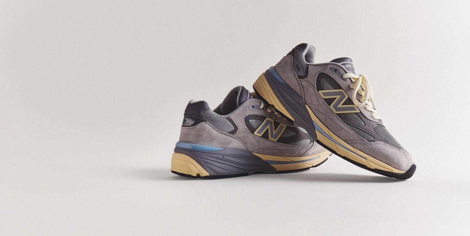 A pair of grey 990v7 sneakers sitting on a grey studio backdrop.