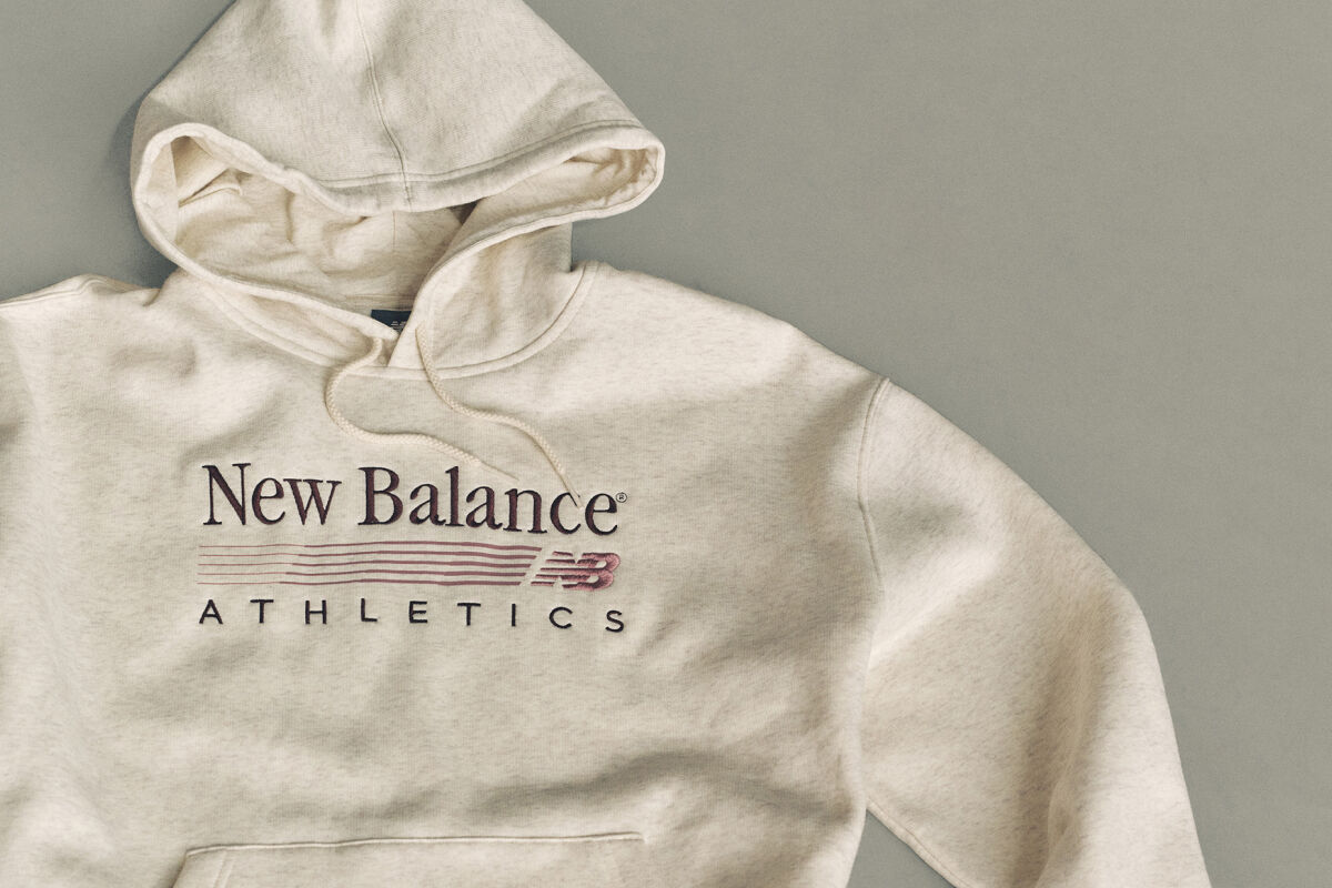 Flat lay studio image of a light beige hooded sweatshirt placed on a smooth, light gray background.