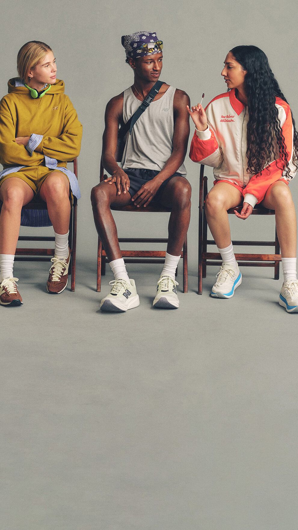 Three people seated side-by-side on simple wooden chairs against a plain, neutral background, arranged in a horizontal line.