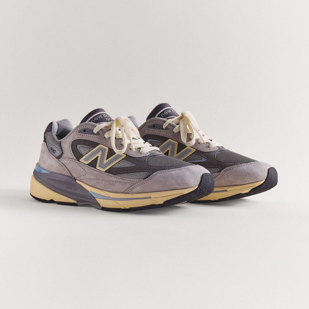 A pair of grey 990v7 sneakers sitting on a grey studio backdrop.