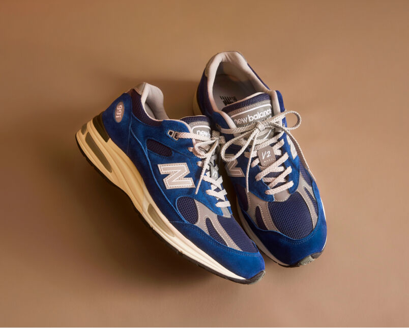 A pair of New Balance Made in UK sneakers in front of a rabbit in a brown textured studio environment. 