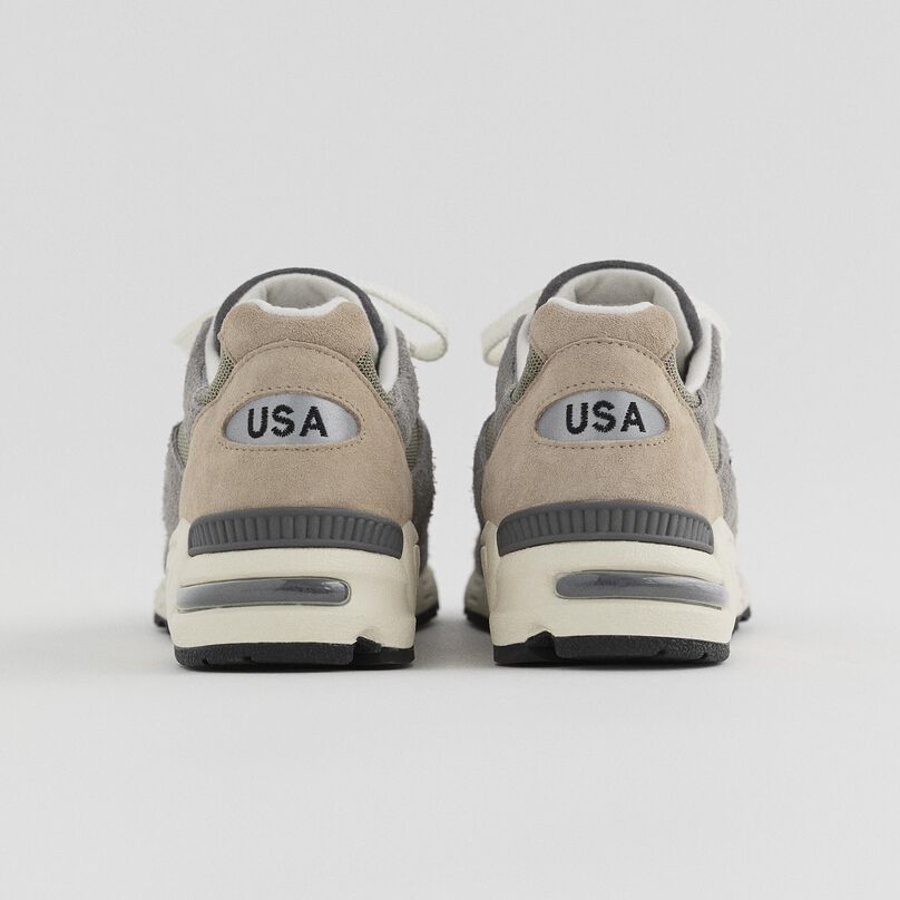 Pair of grey 990v2 pointing away from camera and showing the USA text on the heel of the shoe.